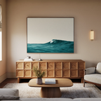 A modern living room with a wooden sideboard, low coffee table, light sofa, and coastal decor. Above the sideboard hangs the Oceanside Crest Canvas Art featuring a wave. A small vase of flowers decorates the coffee table.
