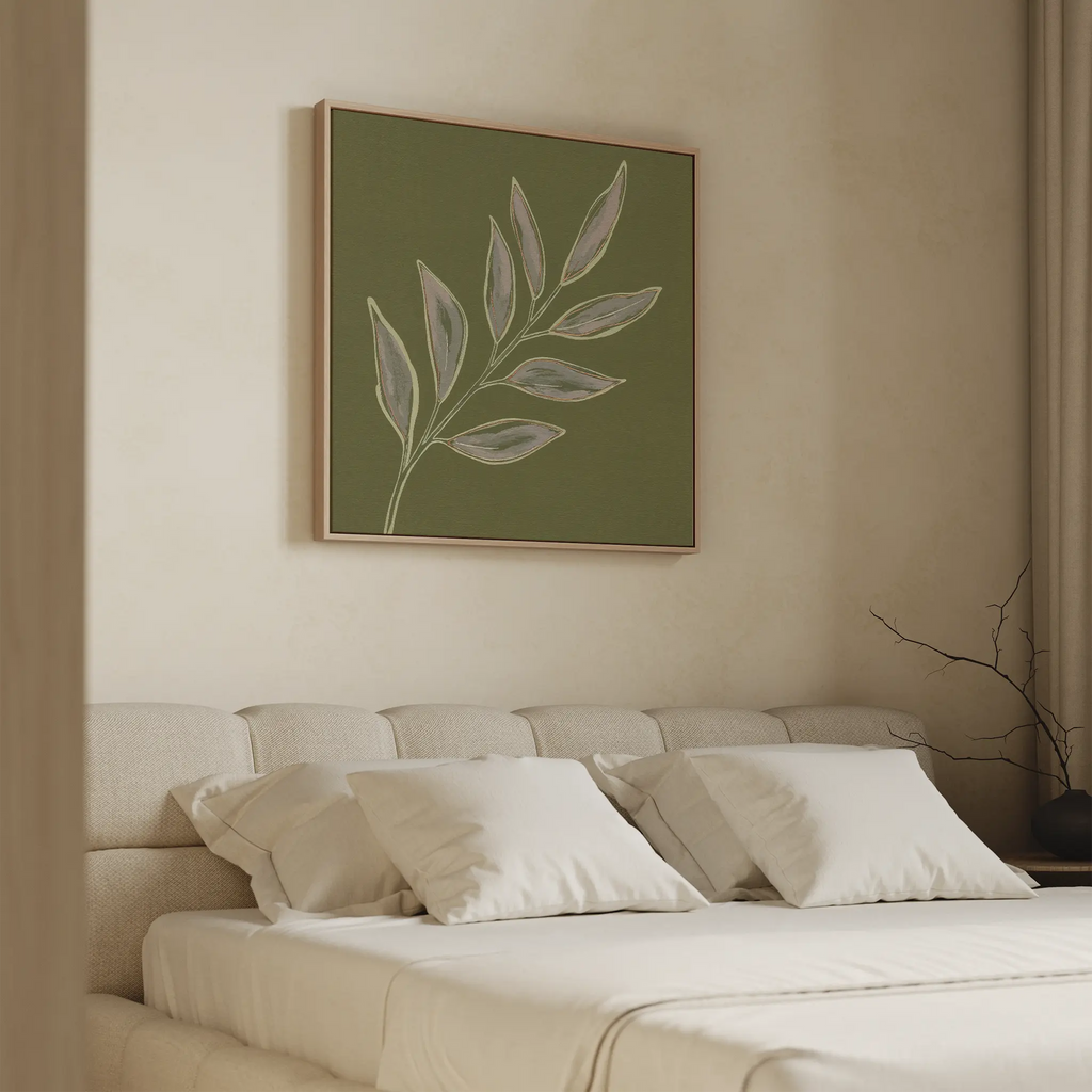 A minimalistic bedroom features a beige upholstered bed with white pillows and the Olive Branch Canvas Art hanging above the headboard. Light walls and simple decor create a calm, cozy atmosphere.