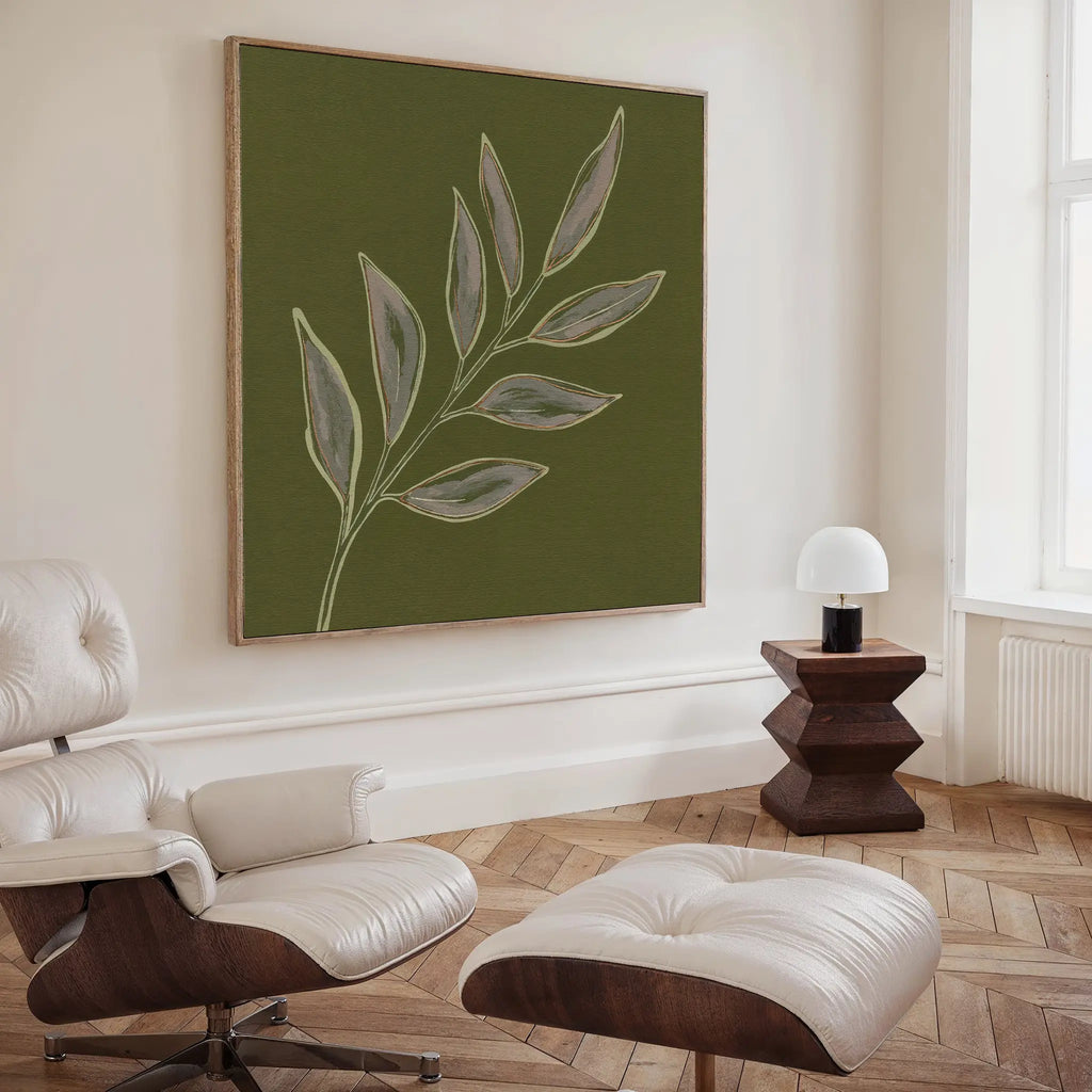 A modern living room features a white leather lounge chair and ottoman, a wooden side table with a white lamp, and the Olive Branch Canvas Art above. Light wood herringbone floors and white walls complete the space.