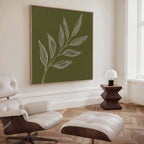 A modern living room features a white leather lounge chair and ottoman, a wooden side table with a white lamp, and the Olive Branch Canvas Art above. Light wood herringbone floors and white walls complete the space.