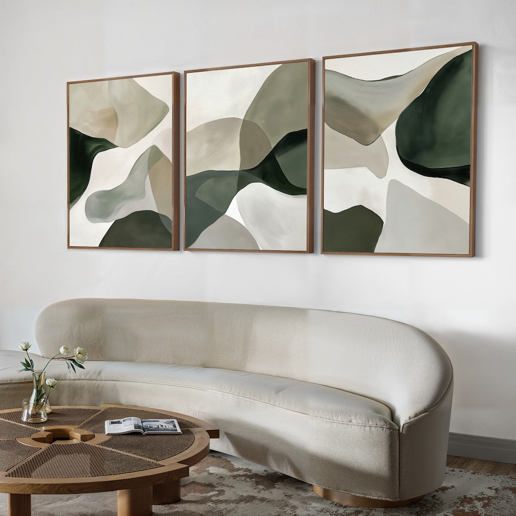 A modern living room with a curved beige sofa, round wooden coffee table, and the Organic Flow Set of 3 abstract green and beige paintings above the sofa. A small vase with flowers completes this cozy, contemporary space.