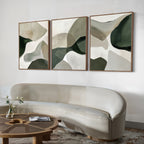 A modern living room with a curved beige sofa, round wooden coffee table, and the Organic Flow Set of 3 abstract green and beige paintings above the sofa. A small vase with flowers completes this cozy, contemporary space.
