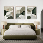 A modern bedroom featuring an olive green bed, white bedding, beige nightstands with matching lamps, and the Organic Flow Set of 3 abstract green and beige paintings displayed above the bed.