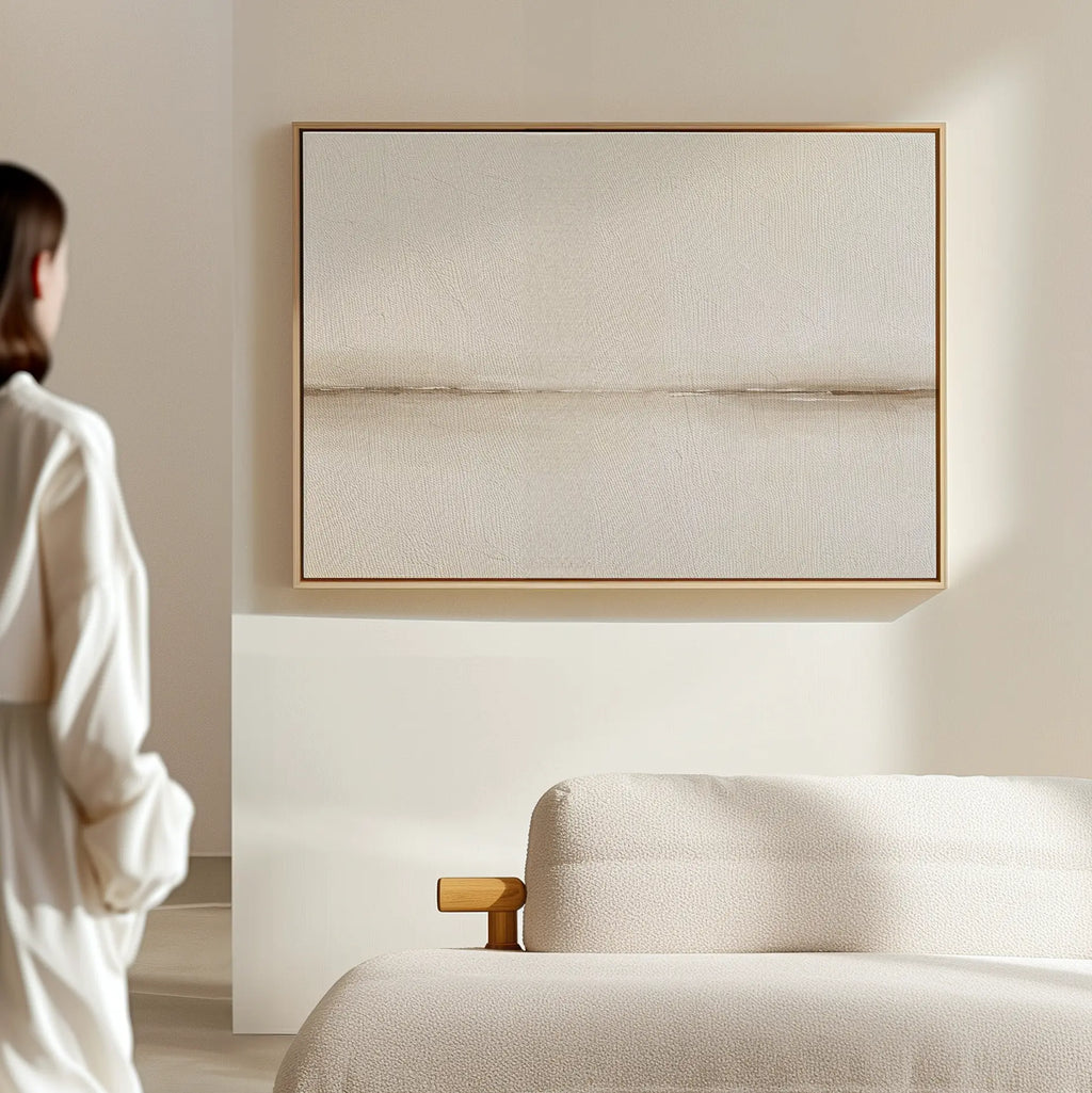 A person in a minimal, modern room admires the Pale Desert Canvas Art above a light-colored sofa—an inspiring touch that elevates elegant living room decor with neutral, minimalist style.