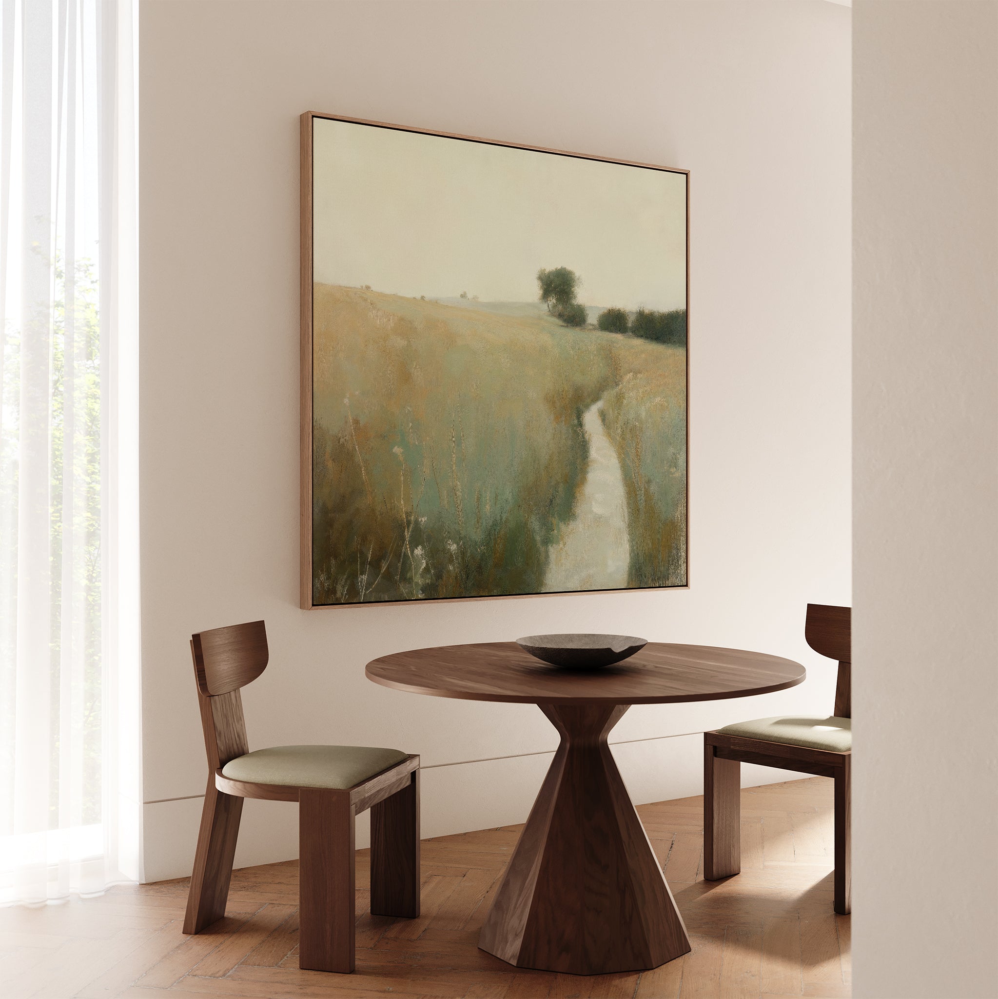 A minimalist dining area features a round wooden table, two cushioned chairs, and rustic decor with the Path Through the Meadow Canvas Art landscape. Soft natural light through sheer curtains creates a serene setting for nature lovers.