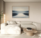 A modern living room with a light beige sectional sofa, wooden coffee table, potted plant, and the Peaceful Waters Canvas Art – Horizontal in soft blue and gray tones creates a tranquil living room decor.