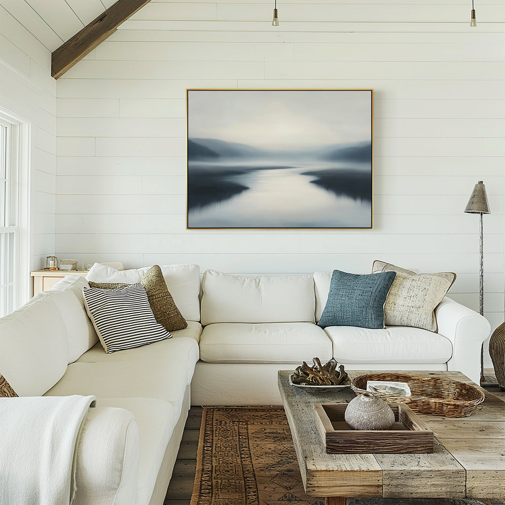 A bright, cozy living room with white shiplap walls, a white sectional, wooden coffee table, and assorted pillows features the Peaceful Waters Canvas Art – Horizontal above the couch for tranquil decor.