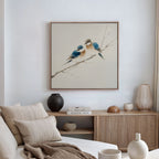 A cozy modern living room with a beige sofa and cushions, a wooden sideboard with books and vases, and the Perched Companions Canvas Art—a framed painting of two bluebirds—adding Nordic wall decor charm above.