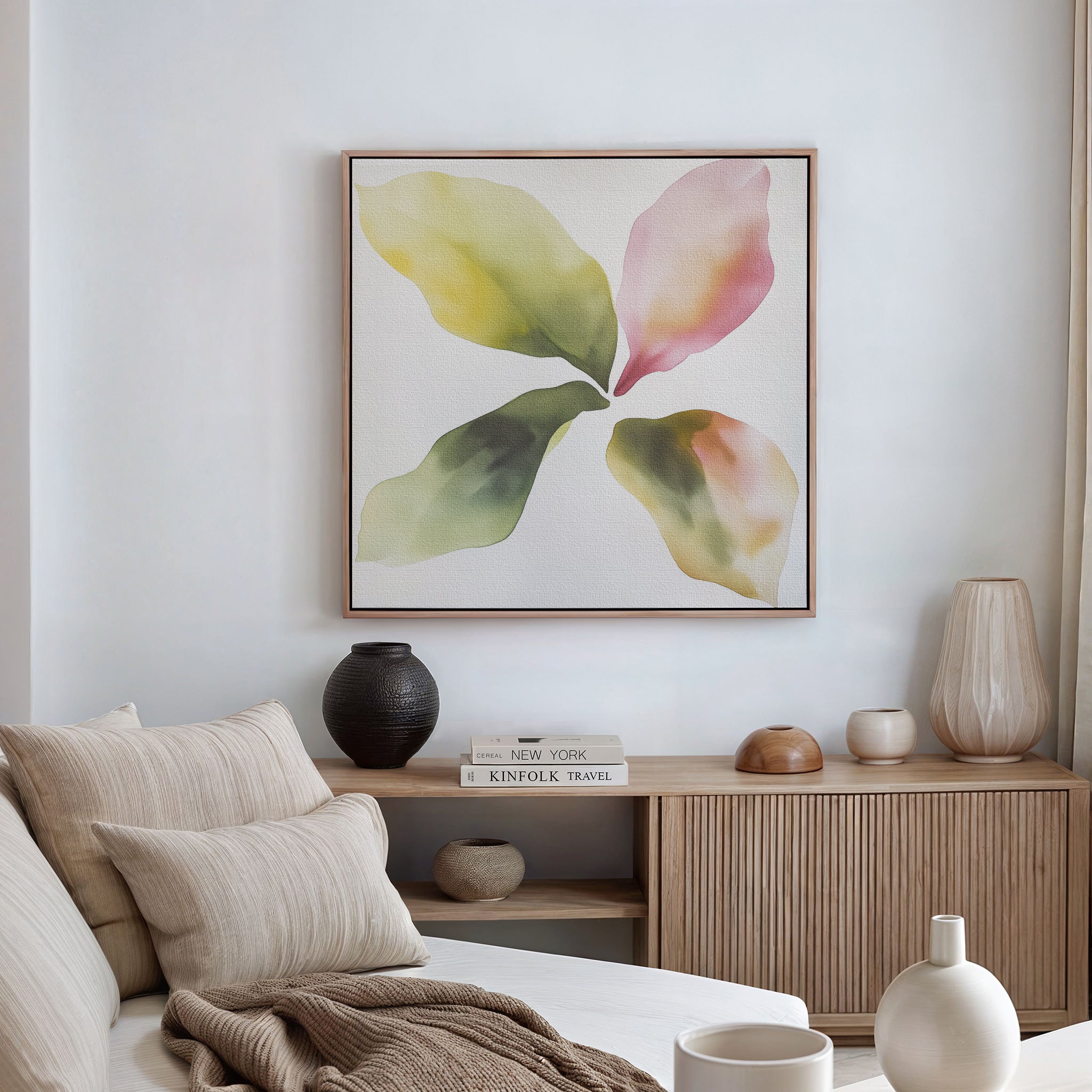 A modern living room featuring a neutral sofa, striped cushions, light wood cabinet, decorative accents, and the Petal Hues Canvas Art—a large abstract floral print in soft greens, yellows, and pinks—displayed on a white wall.
