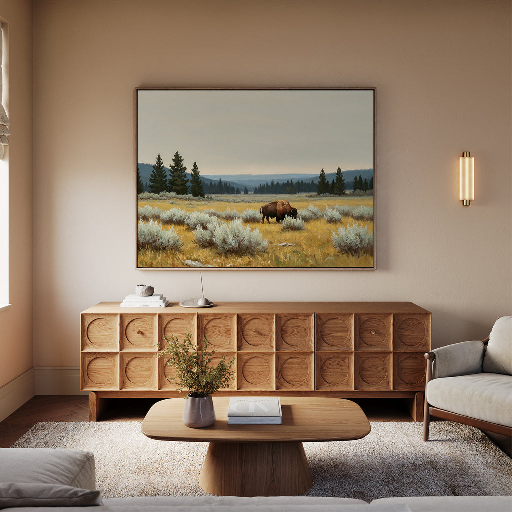 A cozy living room with a wooden sideboard, coffee table, beige sofa, and the Prairie Silence Canvas Art featuring a bison in a grassy field above the sideboard. A vase with flowers on the table completes the nature-inspired decor.