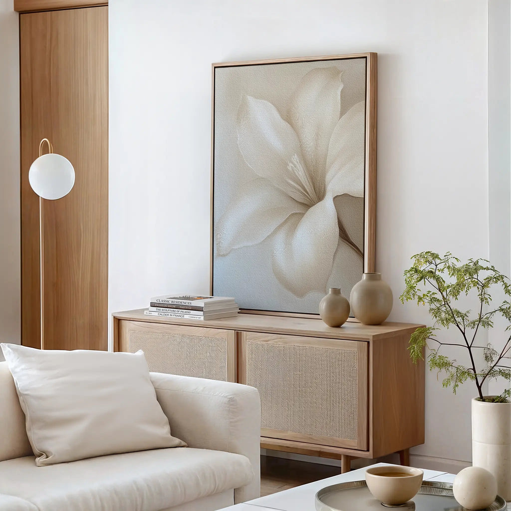 A modern living room with a light wood sideboard, neutral ceramic vases, the Pure Magnolia Canvas Art as minimalist wall decor, a white sofa with cushions, a small glass coffee table, and a potted plant beside the furniture.
