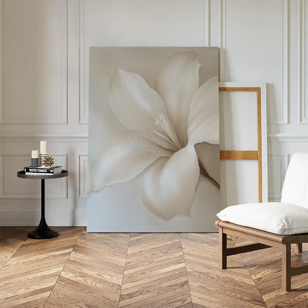 The Pure Magnolia Canvas Art leans against a white-paneled wall beside an empty canvas, complemented by a small round table with candles and books and a wooden chair—ideal for serene bedroom decor on herringbone flooring.