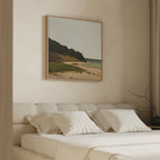 A cozy, minimal bedroom features a beige bed, white pillows, and Quiet Bend Canvas Art—a serene landscape with beach and greenery—above the headboard. Neutral walls and simple decor complete the calm, tranquil vibe.
