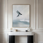 A minimalist console table sits against a beige paneled wall, topped by the Quiet Flight Canvas Art featuring a bird in flight over misty clouds, adding elegance and Nordic Park-inspired charm to the space.