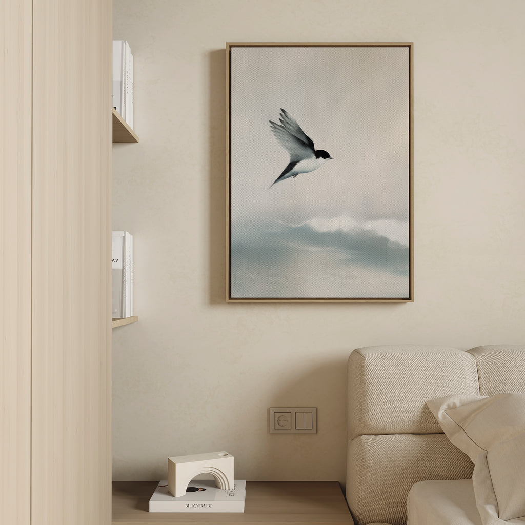 The Quiet Flight Canvas Art, featuring a bird soaring above clouds, is displayed on a beige wall above a light sofa in a minimalist living room—ideal for those who love serene, modern wall decor.