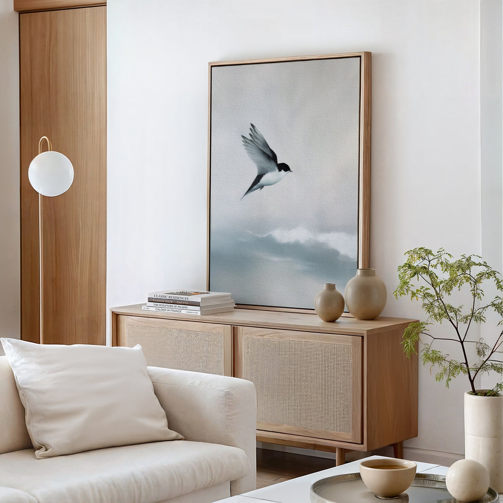 A modern living room in neutral tones features a wooden sideboard with ceramic vases, books, minimalist decor, and the Quiet Flight Canvas Art—a large print of a flying bird above clouds. A potted plant and cream armchair complete the Nordic Park-inspired look.