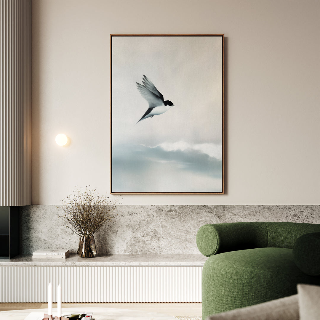 A modern living room with a green curved sofa, marble shelf, minimalist wall decor, a vase with dried branches, and the Quiet Flight Canvas Art featuring a flying bird against a soft, cloudy sky on the wall.