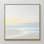 Quiet Shores Canvas Art features a minimalist seascape with soft pastels, a pale sky, and gentle clouds. Framed in thin gold and displayed on a white wall, its perfect coastal decor for any space.