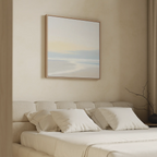 A minimal, modern bedroom features a beige upholstered bed with white bedding. Quiet Shores Canvas Art hangs above, enhancing the serene vibe, while soft natural light and beige curtains complement the tranquil coastal decor.