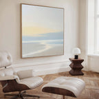 A modern, minimalist room features a white leather lounge chair with ottoman, a geometric side table with dome lamp, and the Quiet Shores Canvas Art above light wood herringbone floors, adding an elegant touch of coastal decor.