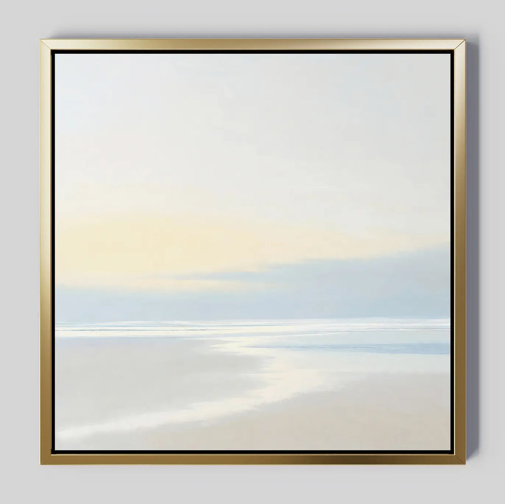 Quiet Shores Canvas Art features a minimalist seashore scene with pale sand, soft pastel sky, and shallow water. Framed in thin gold and set against a light background, its perfect for coastal decor.