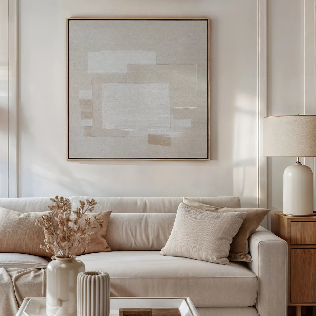 A modern living room featuring a beige sofa, neutral pillows, a wooden side table with a ceramic lamp, and Quiet Structure Canvas Art in soft tones. A vase with dried flowers on the coffee table completes the minimalist decor.