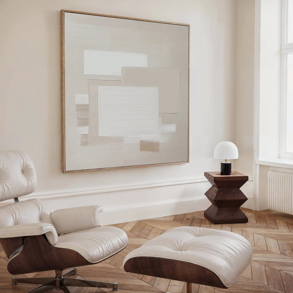 A modern, minimalist room with a cream leather lounge chair and ottoman, a dark wood side table with a white lamp, and striking neutral wall art—the Quiet Structure Canvas Art—displayed as a large abstract painting on the wall.