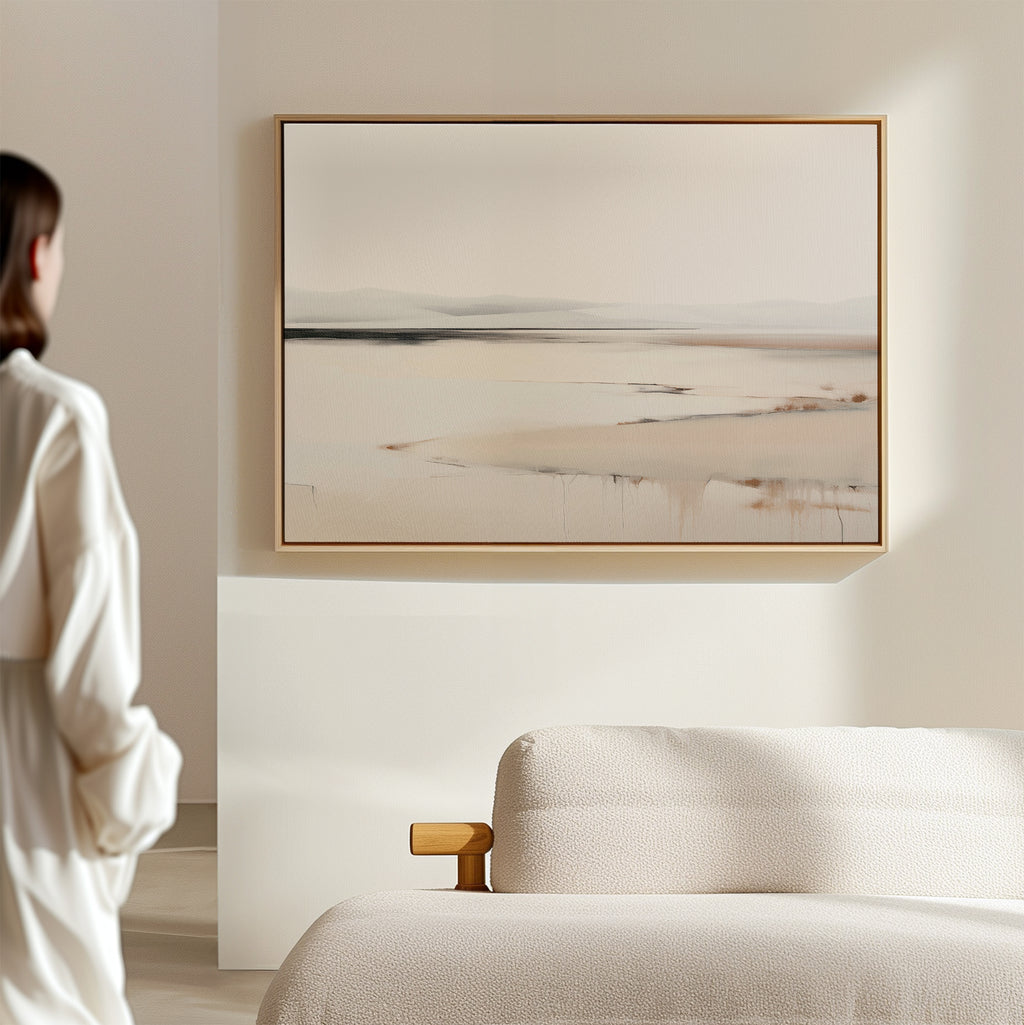 A person in a white shirt stands in a minimalist room, admiring the Quiet Valley Canvas Art – Horizontal, an abstract landscape wall print that adds elegant simplicity above the cream-colored sofa—ideal for refined living room decor.