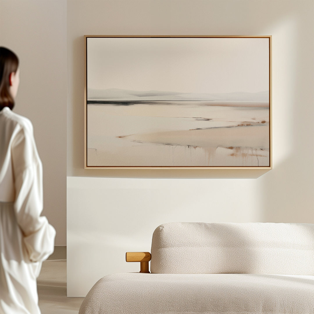 A person in a white shirt stands in a minimalist room, admiring the Quiet Valley Canvas Art – Horizontal, an abstract landscape wall print that adds elegant simplicity above the cream-colored sofa—ideal for refined living room decor.