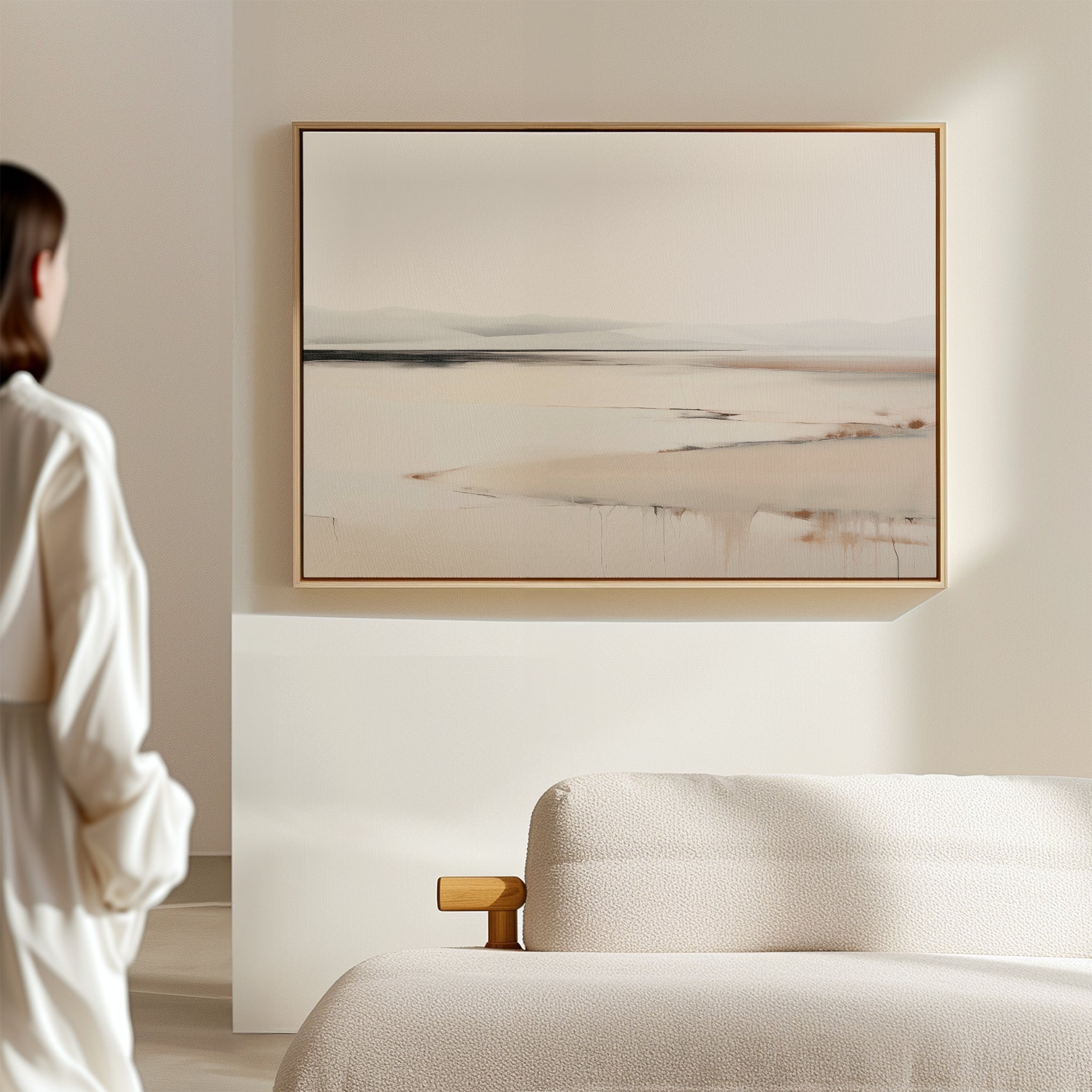 A person in a white shirt stands in a minimalist room, admiring the Quiet Valley Canvas Art – Horizontal, an abstract landscape wall print that adds elegant simplicity above the cream-colored sofa—ideal for refined living room decor.