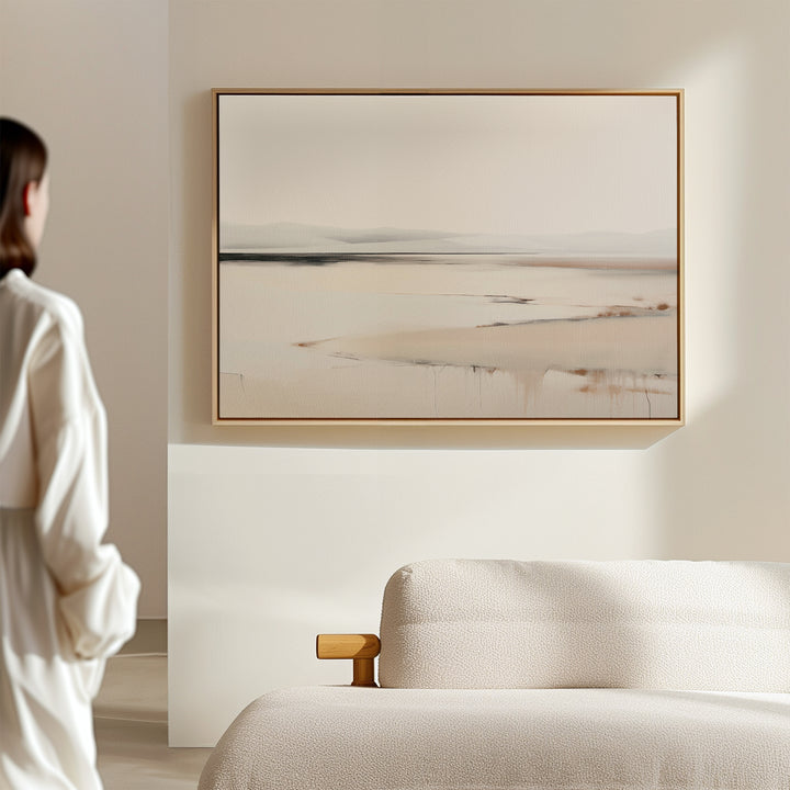 A person in a white shirt stands in a minimalist room, admiring the Quiet Valley Canvas Art – Horizontal, an abstract landscape wall print that adds elegant simplicity above the cream-colored sofa—ideal for refined living room decor.