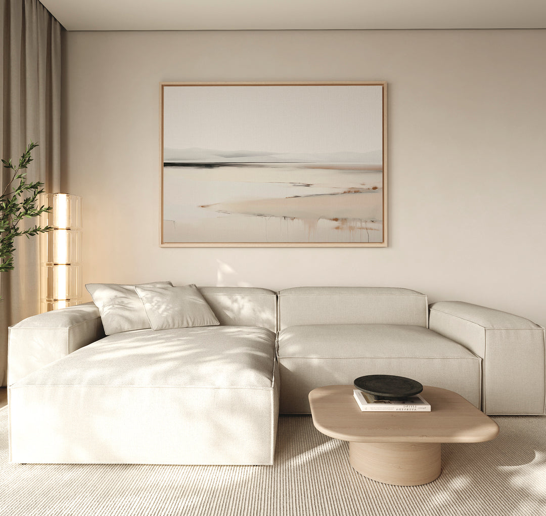 A modern living room features a light beige sectional sofa, wooden coffee table, black bowl, tall plant, and the Quiet Valley Canvas Art – Horizontal. Neutral hues and minimalist elegance create a calm, inviting atmosphere.