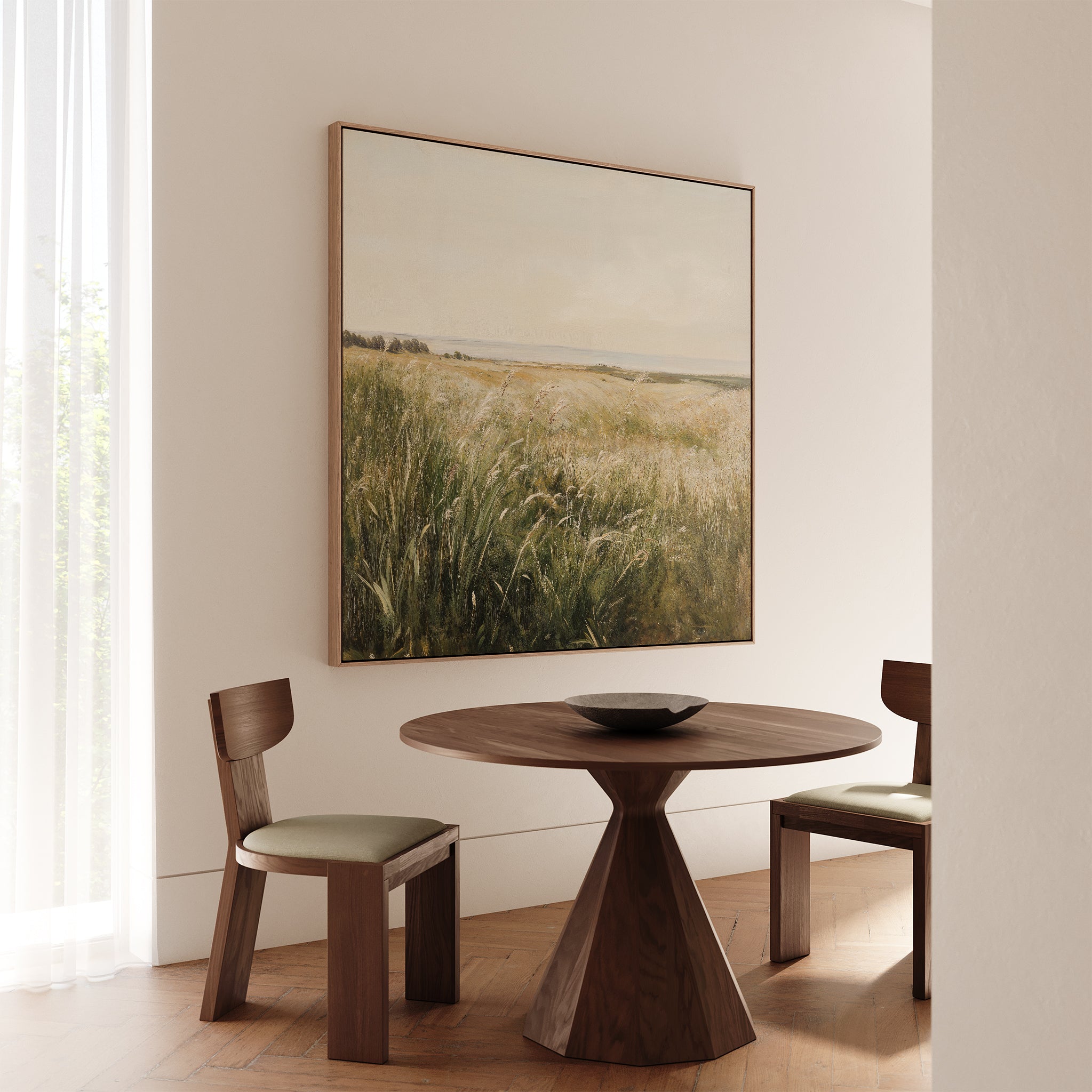 A minimalist dining area features a round wooden table, two cushioned chairs, and the Reeds by the River Canvas Art on a beige wall. Soft natural light through sheer curtains adds warmth to the living room decor.