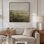 A neutral-toned living room features a white sofa, beige pillows, and vases on a side table. Above the sofa hangs the Reeds by the River Canvas Art, adding serene decor and completing this tranquil space.