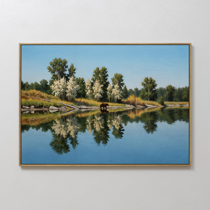 The Reflections of the Wild Canvas Art features a brown bear by a tranquil river, with trees and shrubs mirrored under a clear blue sky—ideal wall art to enhance your minimalist decor with natural charm.