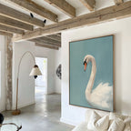A modern living room with exposed wooden beams, white walls, a beige-shaded floor lamp, and a white sofa features the Regal Swan Canvas Art—a framed painting of a swan on blue—as the striking focal point.