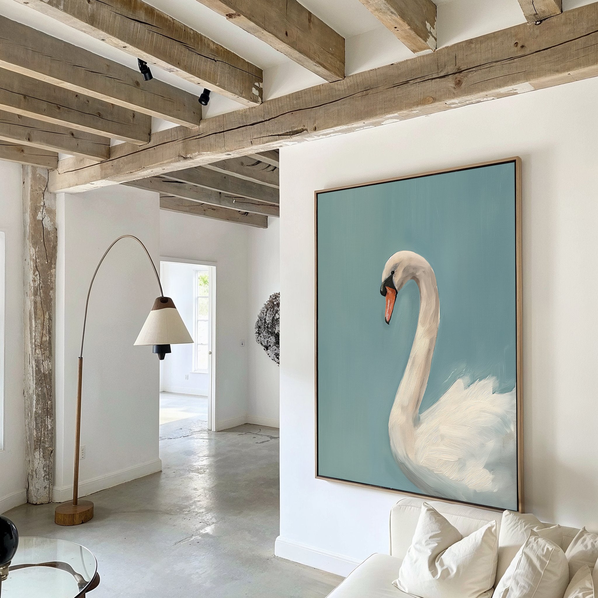 A modern living room with exposed wooden beams, white walls, a beige-shaded floor lamp, and a white sofa features the Regal Swan Canvas Art—a framed painting of a swan on blue—as the striking focal point.