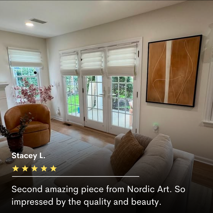 A bright, modern living room with light wood floors, white walls, a tan armchair, and a white sofa. Large windows offer garden views. The Soft Brown Flow Abstract Canvas Art adds minimalist style above a 5-star review.