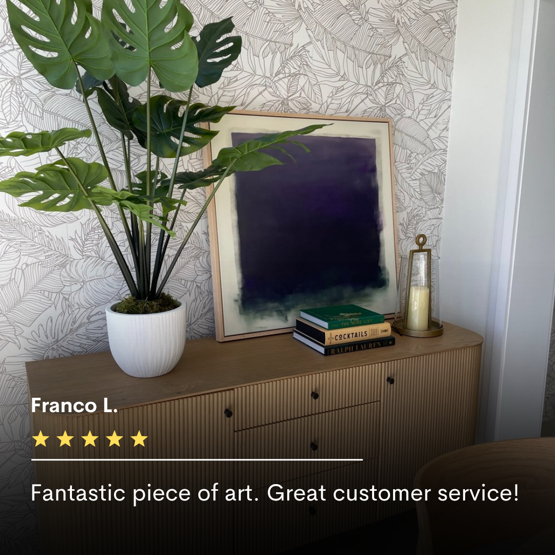 A leafy plant, abstract wall art, candles, and books rest on a wooden sideboard against leaf-patterned wallpaper. A five-star review praises the Deepest Night Canvas Art for its impressive size and excellent customer service.