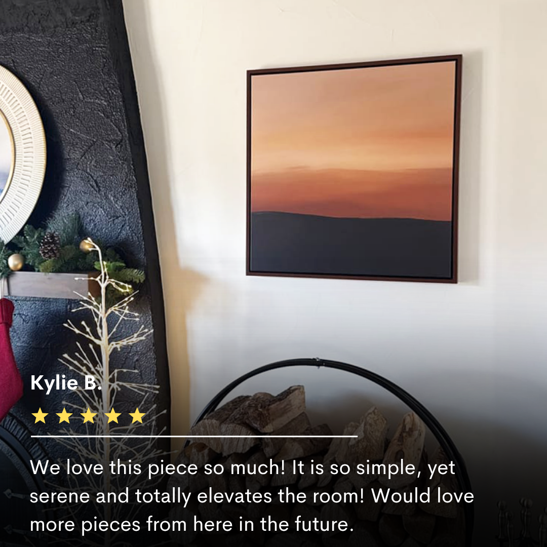 The Tranquil Vista Abstract Canvas Art, with warm sunset hues, hangs above a round fireplace and stacked firewood. A gold tree and mirror accent the space—stunning living room decor with a five-star review from Kylie B. displayed below.