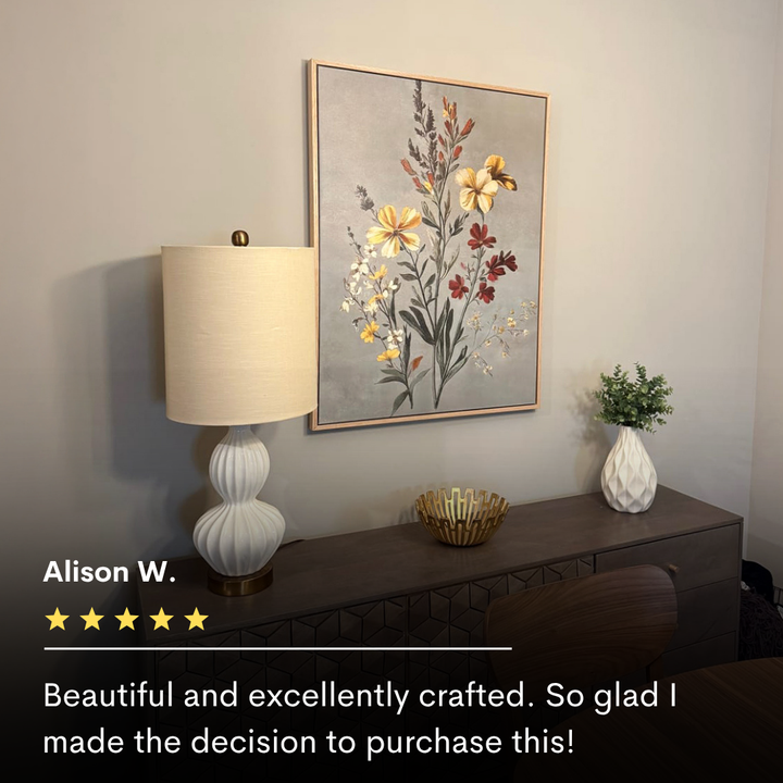 The Velvet Petals Canvas Art hangs above a modern sideboard with a white lamp, gold bowl, and greenery-filled vase. Alison W.’s five-star review praises the artwork’s beauty and quality.