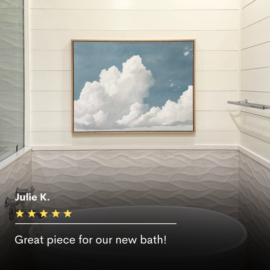 A bathroom with textured tile walls, a glass shower door, and a towel bar. The Soaring Peace Canvas Art showing white clouds on blue sky hangs above the bathtub, with review text and a five-star rating overlaid at the bottom.