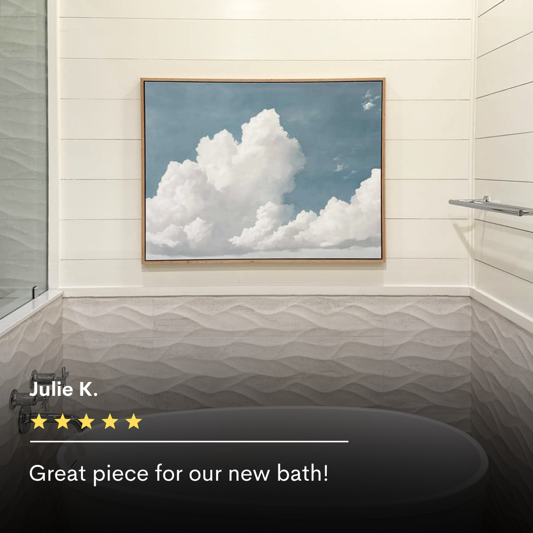 A bathroom with textured tile walls, a glass shower door, and a towel bar. The Soaring Peace Canvas Art showing white clouds on blue sky hangs above the bathtub, with review text and a five-star rating overlaid at the bottom.