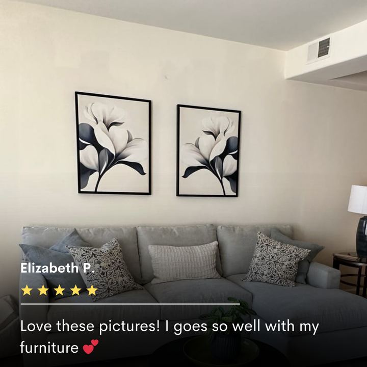 A living room featuring a light gray sofa, patterned pillows, a small plant, table lamp, and striking modern decor with the Navy Magnolia Set of 2 black-and-white floral wall art displayed above the sofa.