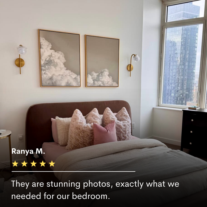 A modern bedroom features a brown headboard, pink and beige pillows, wall sconces, large windows with a cityscape view, and the Clouded Dreams Set of 2 minimalist canvas prints above the bed. A five-star review of the photos is displayed at the bottom.
