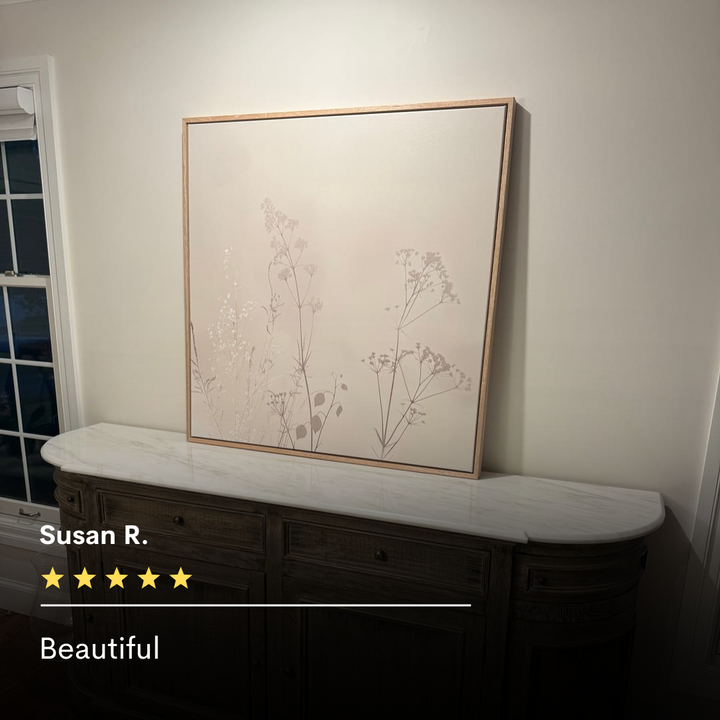 The Floral Symphony Abstract Canvas Art, featuring delicate plant silhouettes, sits on a marble-topped wooden sideboard—perfect minimalist wall art for living room decor. Five-star review from Susan R.: Beautiful.