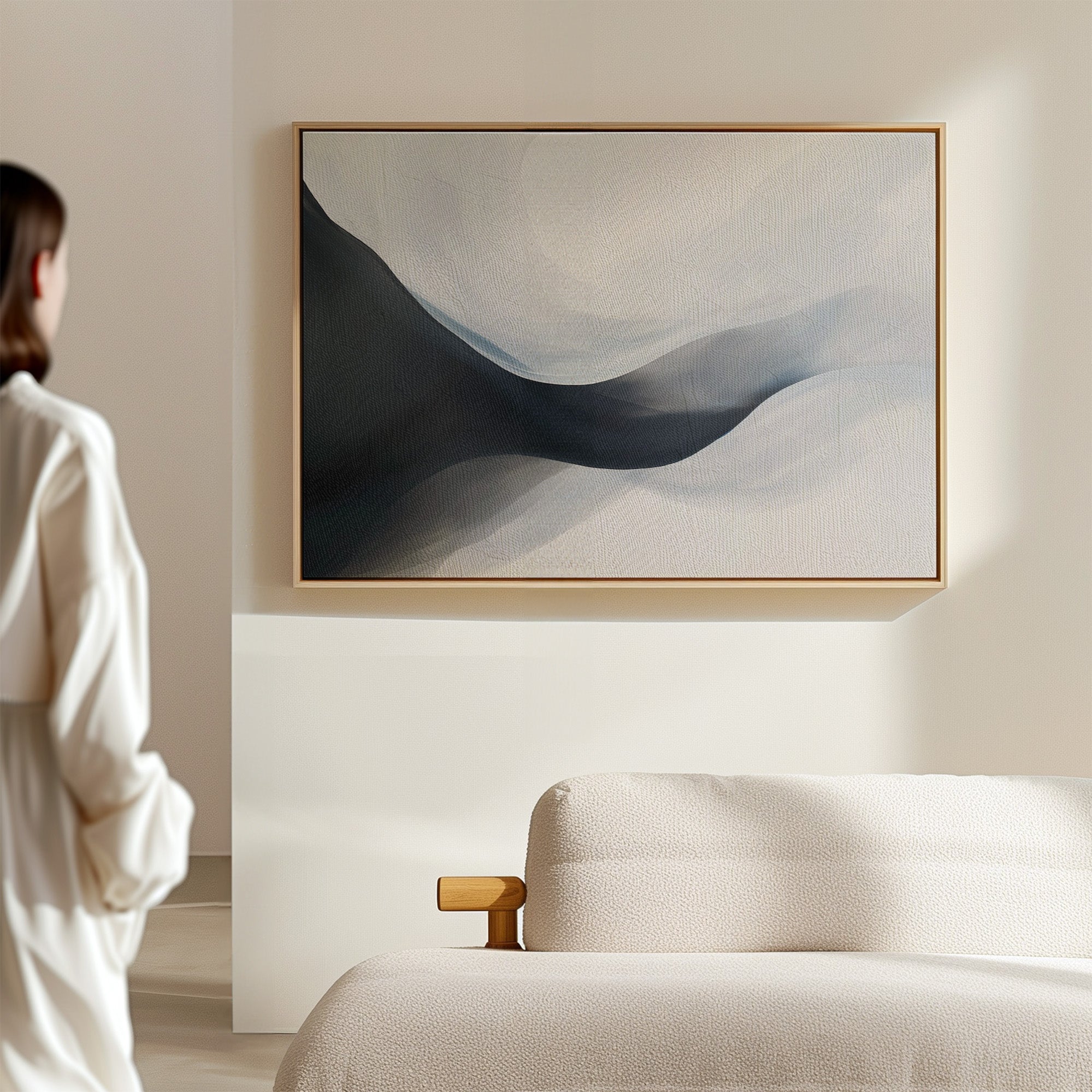 A person stands in a sunlit, minimal room with a beige sofa, admiring the Rippling Vista Abstract Canvas Art—a serene wall print with soft blue and gray shapes that perfectly embodies modern elegance.