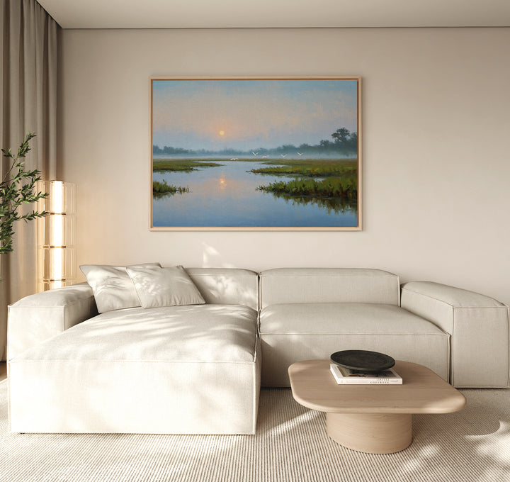 A minimalist living room with a cream-colored sectional sofa, a light wood coffee table, and the Rising Stillness Canvas Art—a striking sunrise over a river—hung above the sofa as a serene focal point.