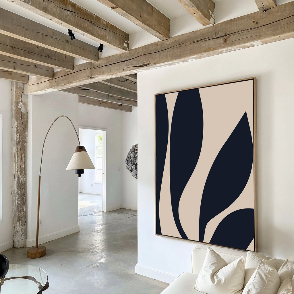 A modern living room with exposed wooden beams, a Dark Blue Leaves Abstract Canvas Art on the wall, a curved floor lamp, white walls, and a cream sofa with pillows—an epitome of modern elegance.