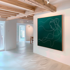 A modern art gallery with white walls and wooden ceiling beams showcases the Azure Silhouette Abstract Canvas Art—a large green minimalist piece featuring an abstract line drawing of a womans profile, illuminated by sunlight streaming through big windows.